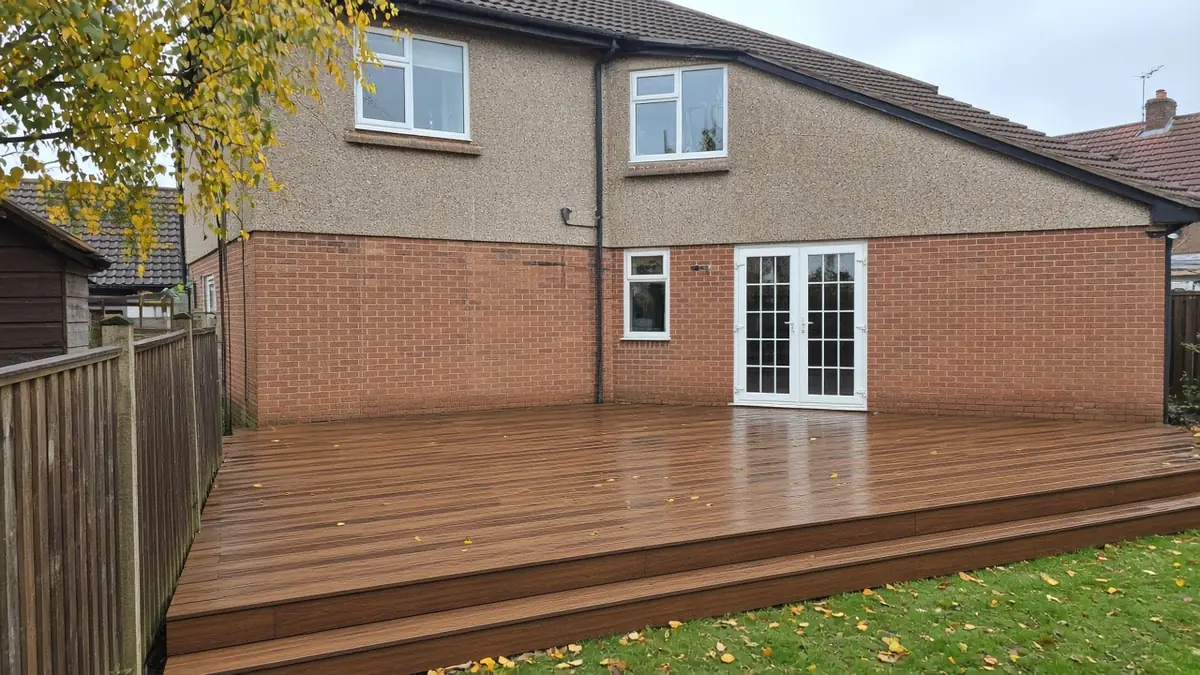 Example image: low walnut-brown composite deck behind a 1930s pebble-dash semi, wet after a shower